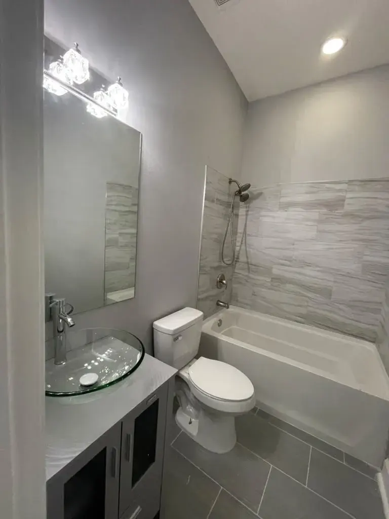 Compact bathroom with a glass vessel sink, a wall mirror, vanity lights and a tub with a tiled surround