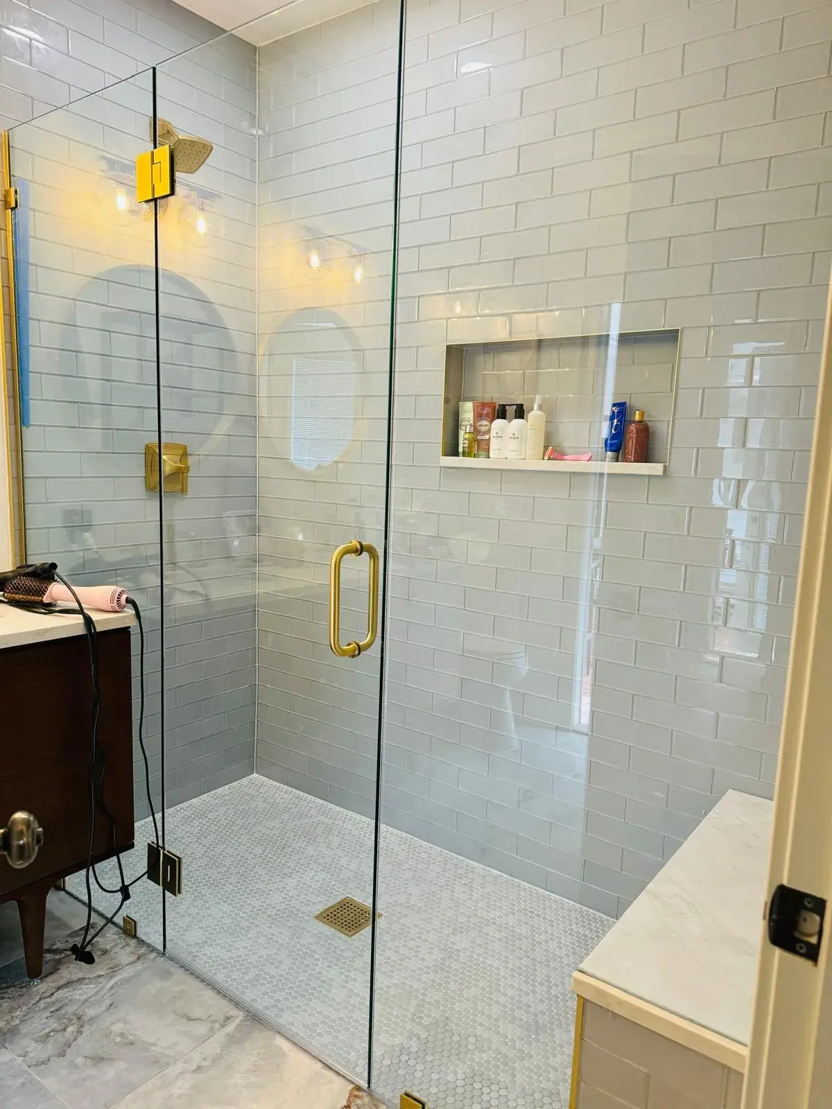 Glass shower with white subway tile, a recessed niche and gold fixtures beside a wood vanity