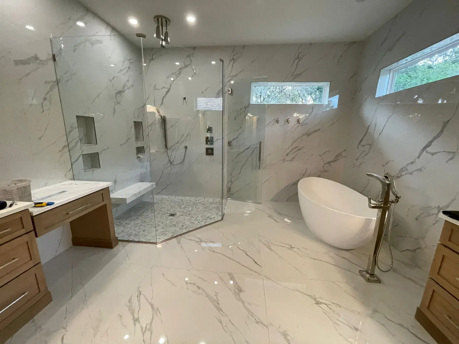 Large bathroom with a freestanding tub, a glass shower and marble-look tile on the floor and walls