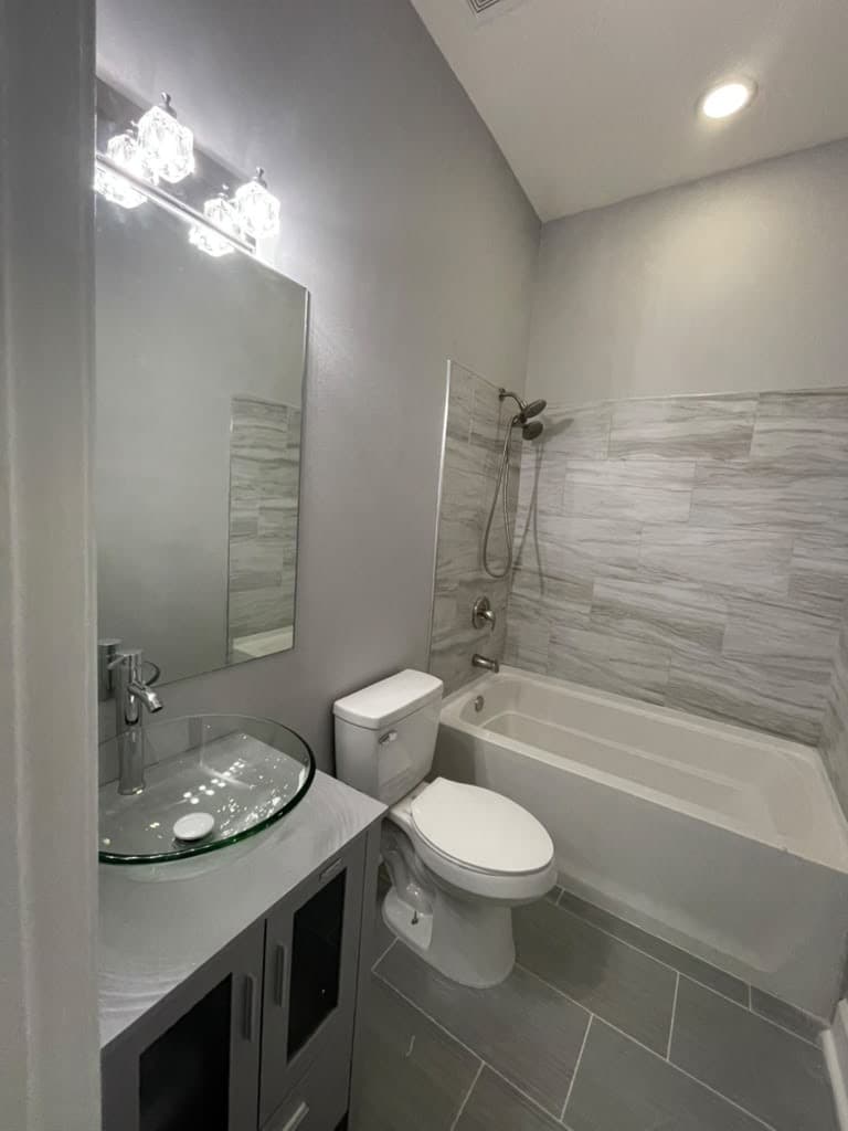 Remodeled bathroom with gray floor tile, tub surround and glass vessel sink