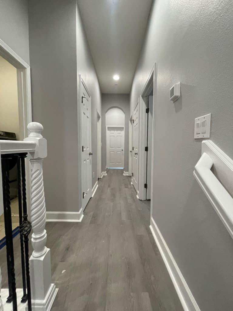 Long hallway with continuous gray plank flooring and white baseboards
