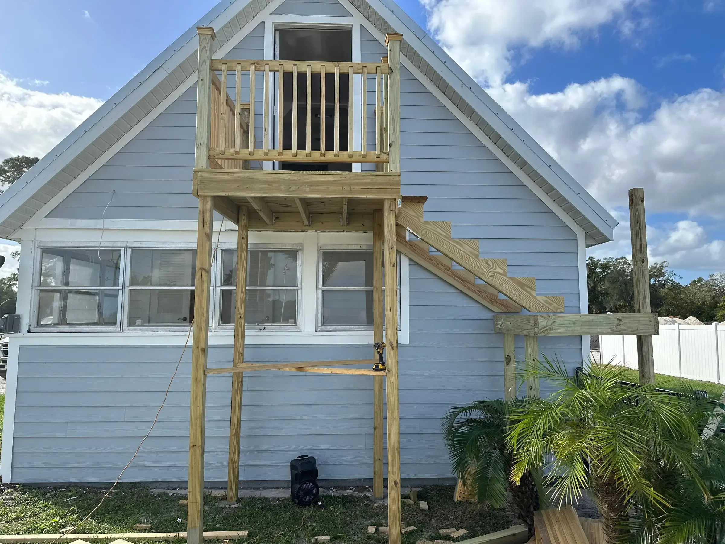 Wood exterior staircase and upper landing under construction against a light blue house, with temporary bracing