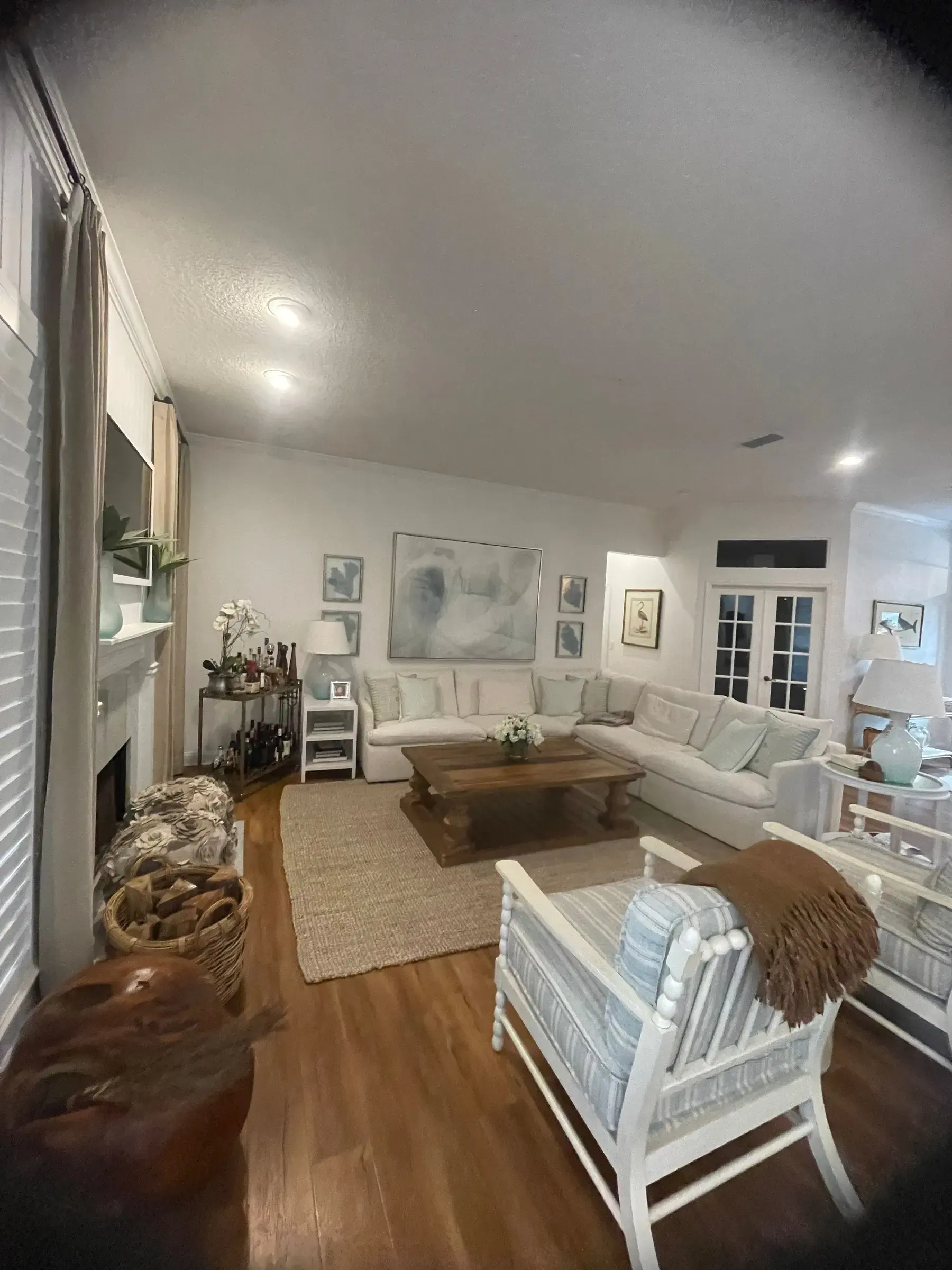 Living room with wood flooring, a white fireplace wall, seating and French doors.