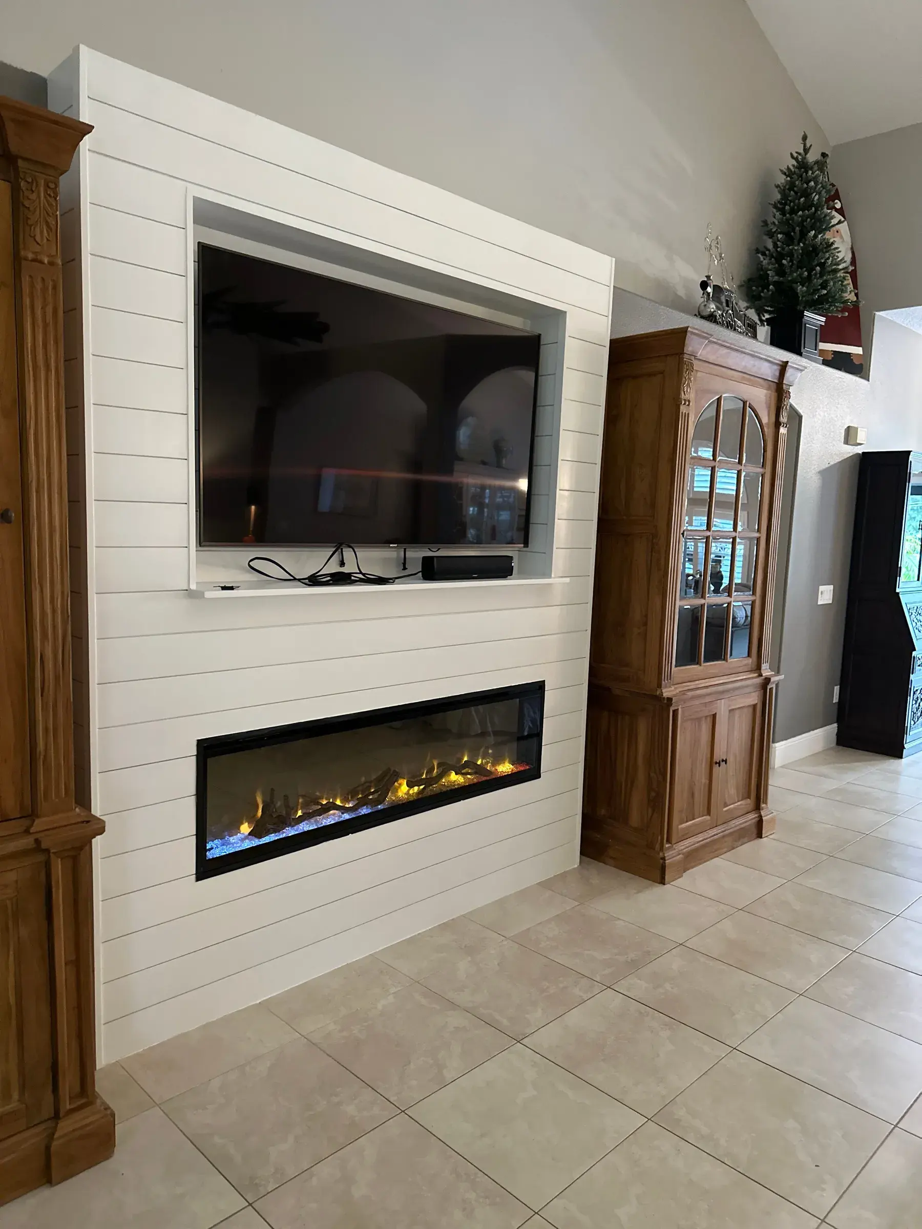 White horizontal-panel TV wall with a recessed TV niche and a linear fireplace, beside wood cabinets and a tile floor