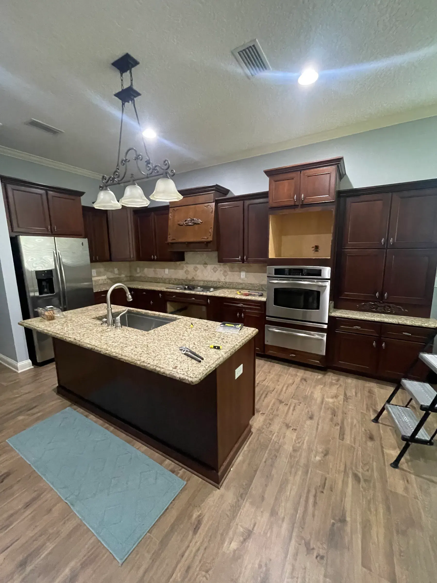 Kitchen with dark wood cabinets, a sink island and an empty appliance niche during installation