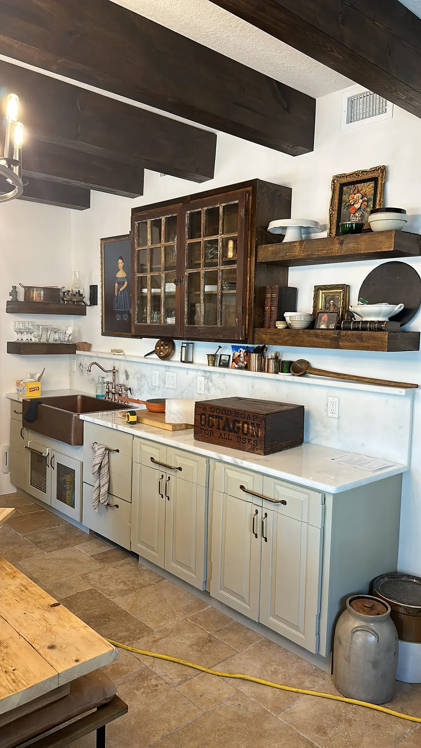 Kitchen cabinetry with a copper-colored sink, light countertop, open shelves and dark wood ceiling beams
