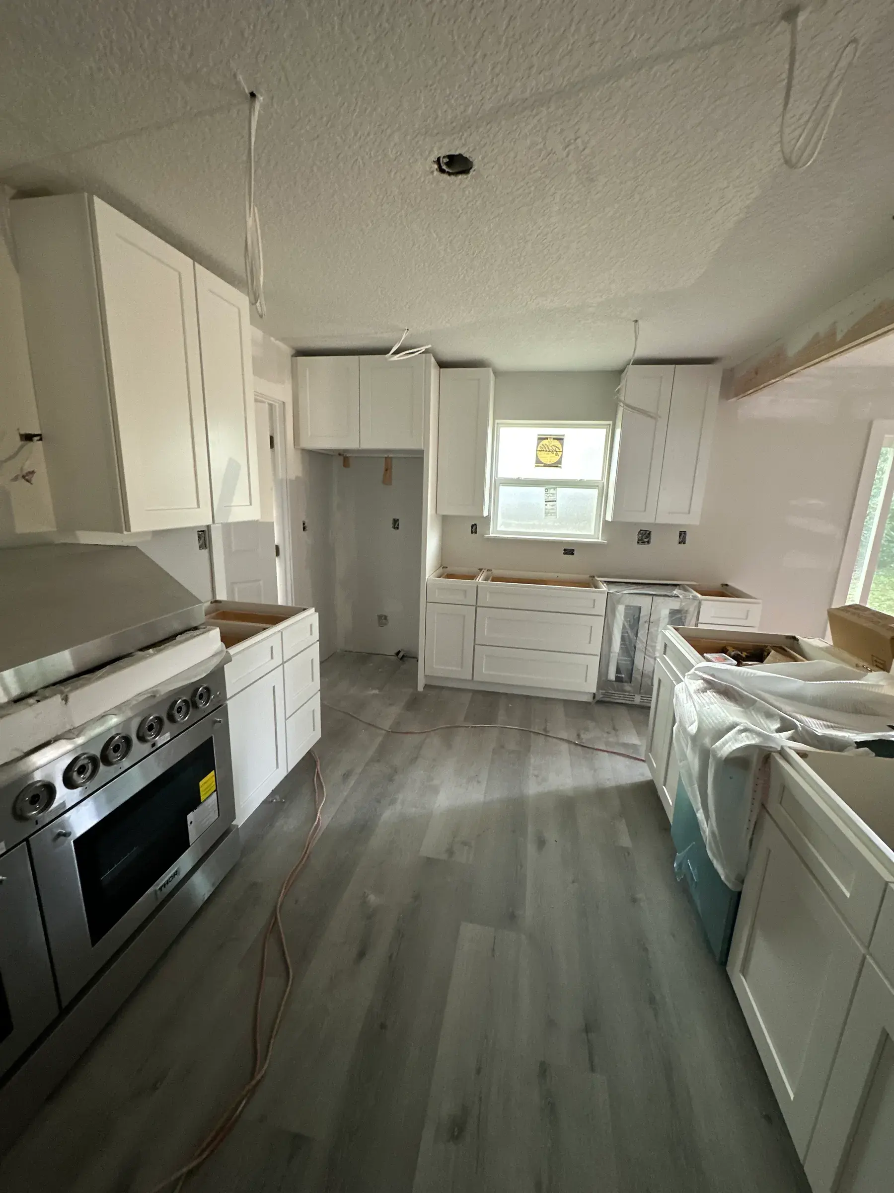 Kitchen with white shaker cabinets, a stainless range and gray plank flooring during installation, with open ceiling wiring