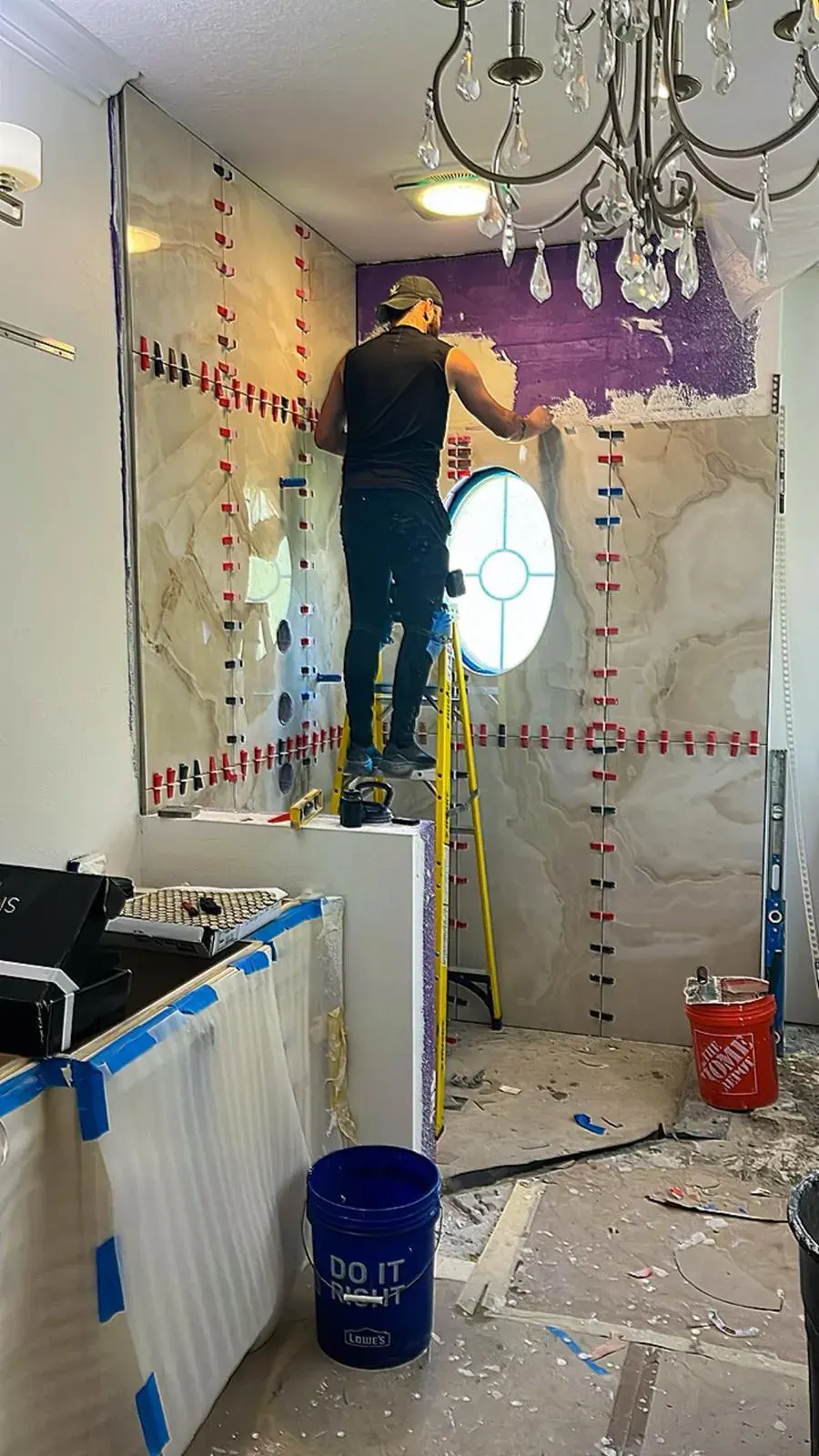 A tile installer setting large marble-look tile around an oval window