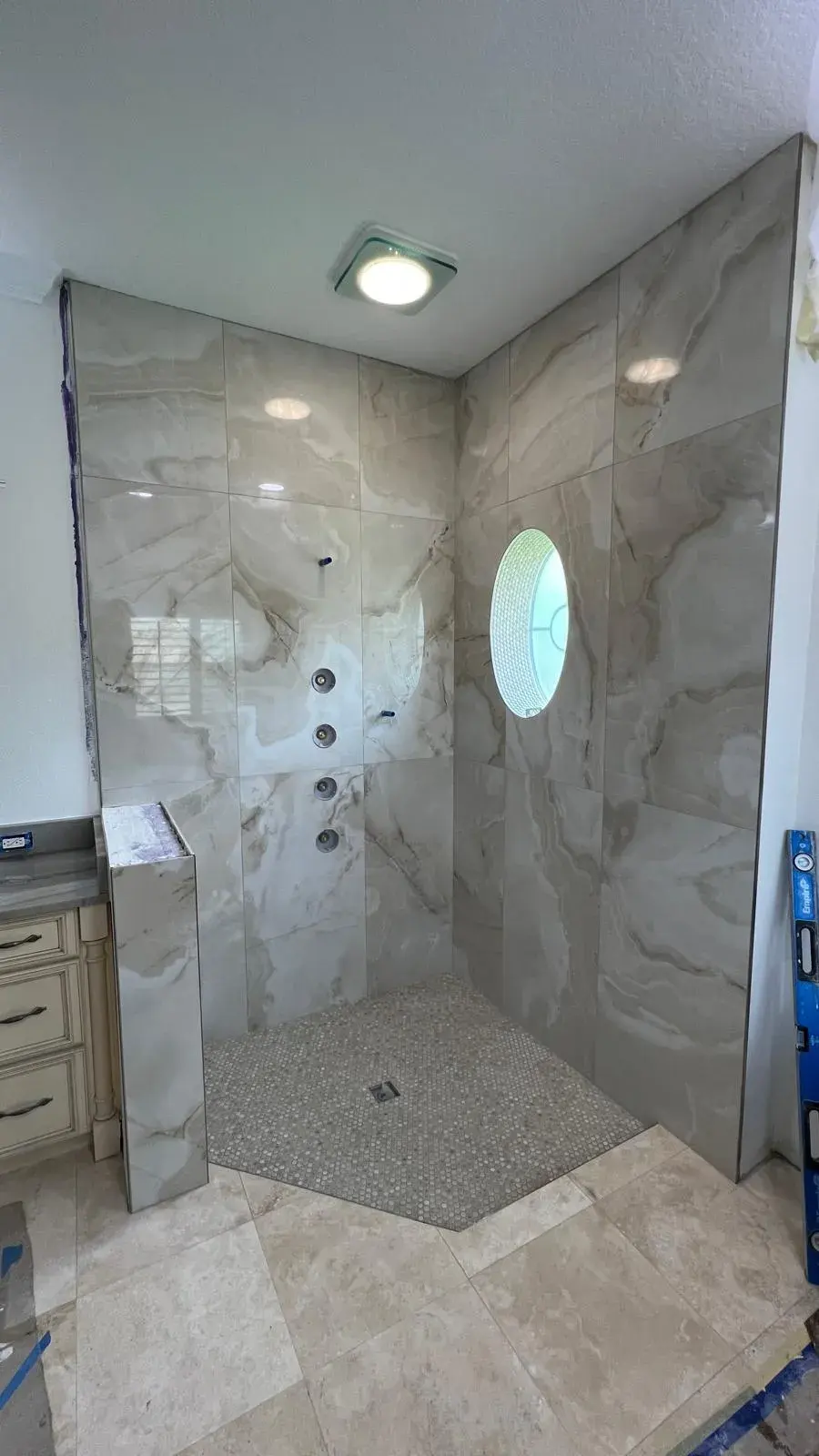 Marble-look wall tile installed around an oval window and a shower floor
