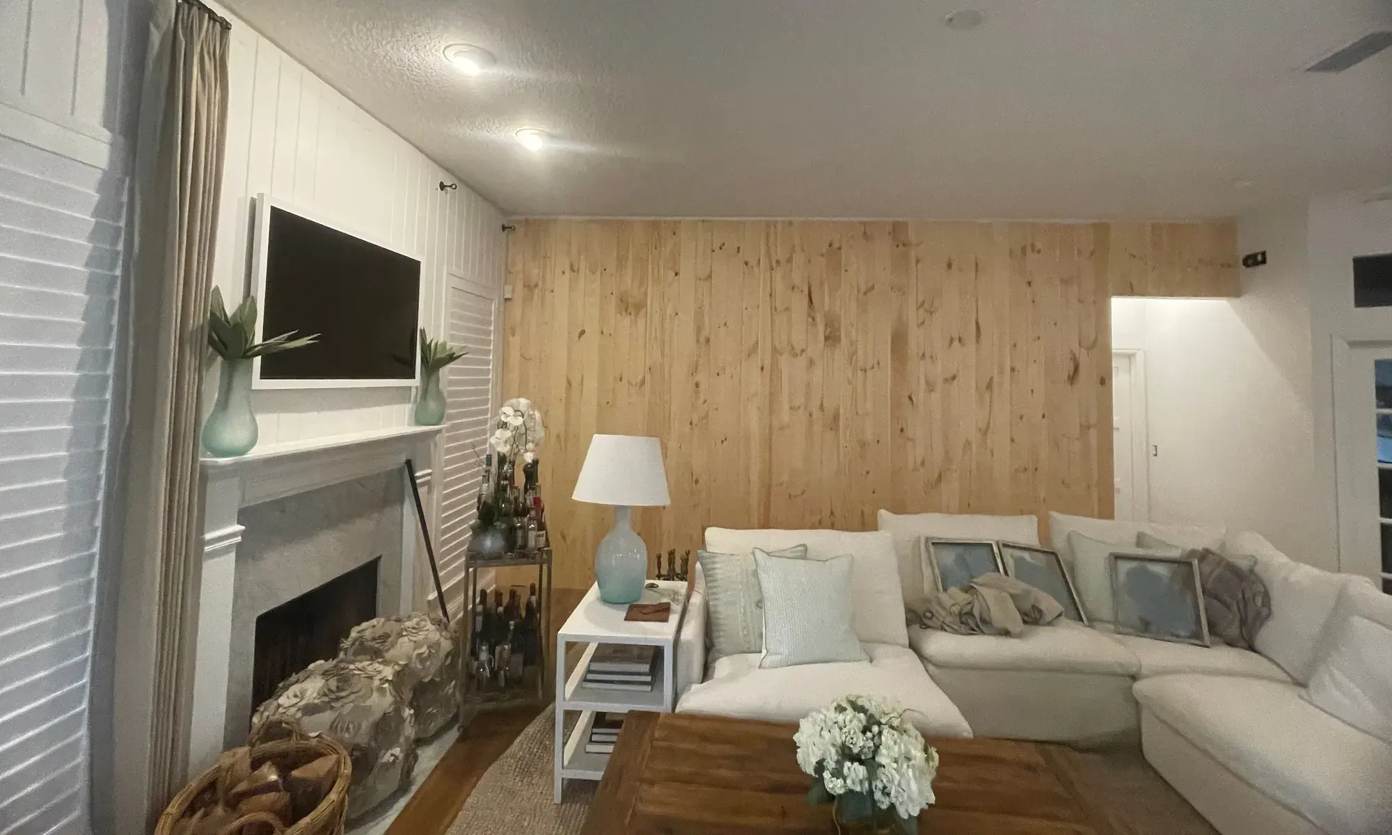 Living room with a natural wood-paneled wall, a white paneled fireplace wall and a sectional sofa