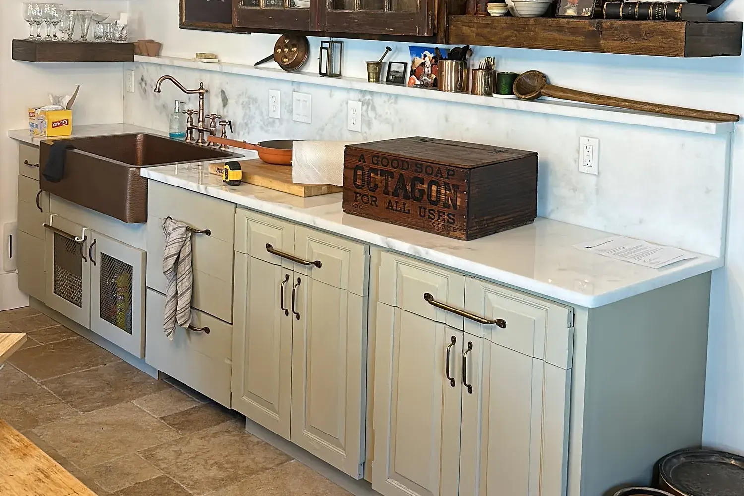 Kitchen cabinetry with a copper-colored sink, light countertop and a tile floor.