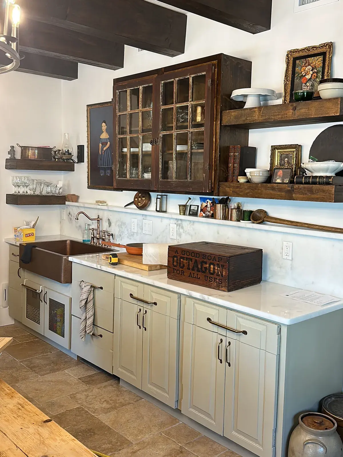 Kitchen cabinetry with a copper-colored sink, light countertop, open shelves and dark wood ceiling beams.