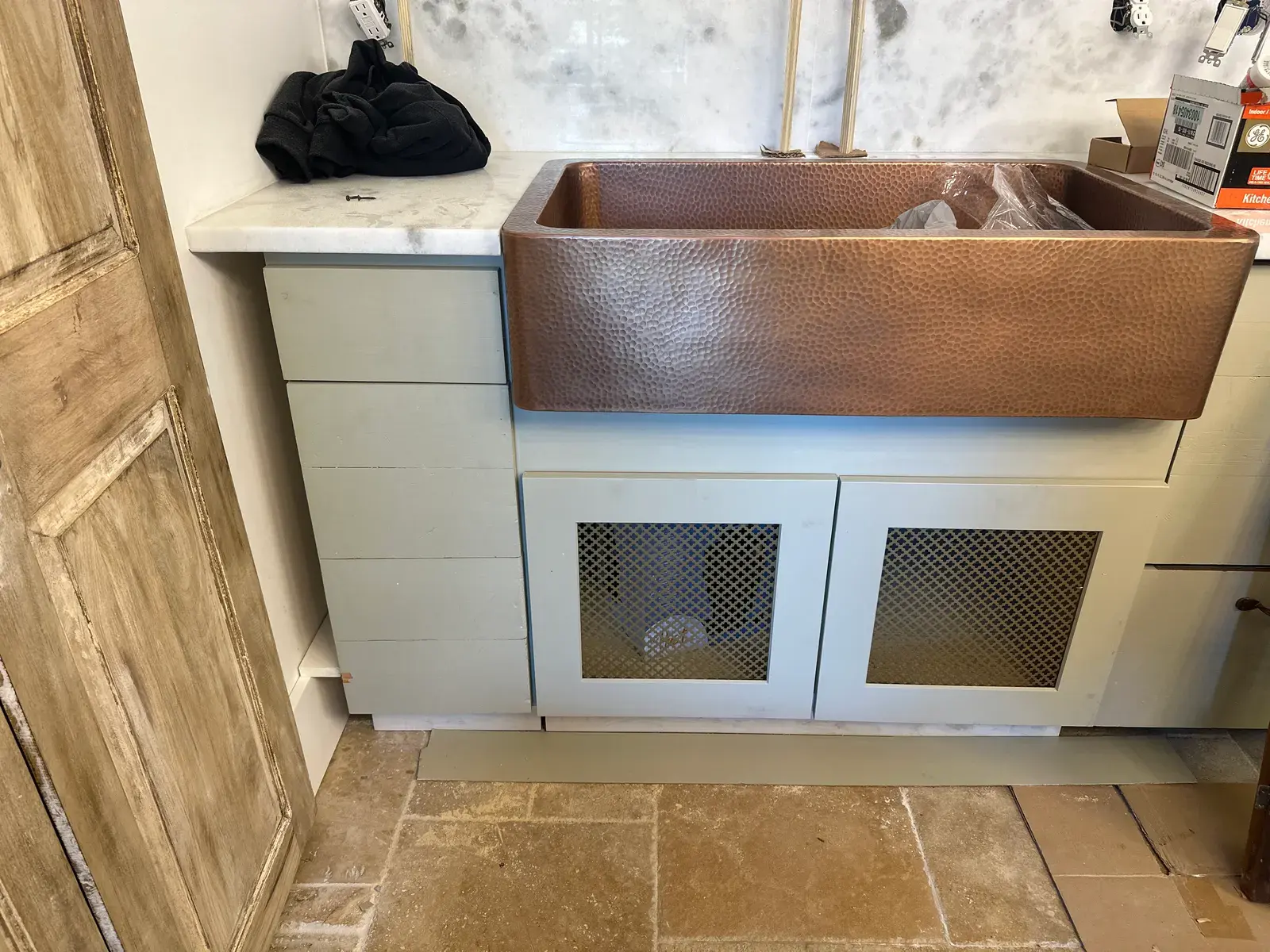 Copper-colored farmhouse sink set into light cabinetry during installation